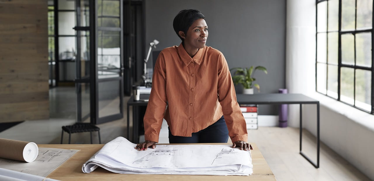 An entrepreneur stands in her office space, looking thoughtfully out a window