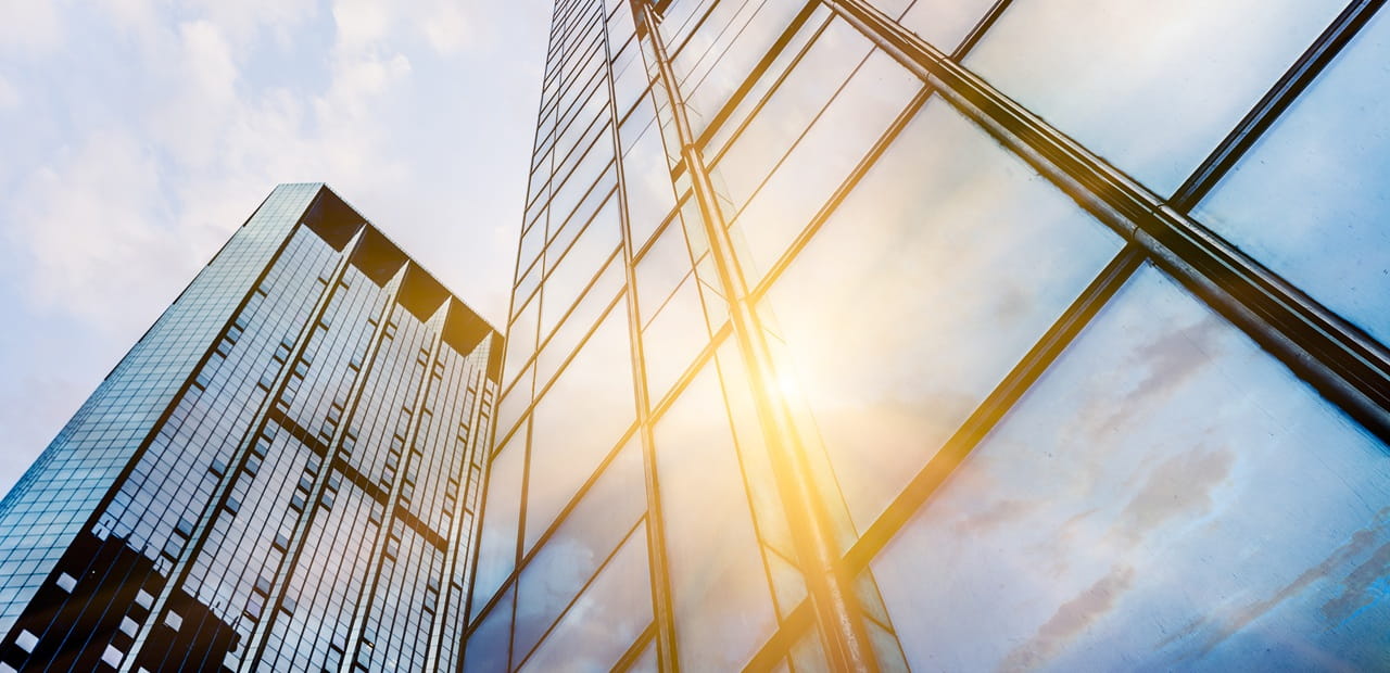 Upward view of modern glass skyscrapers reflecting sunlight and blue sky.