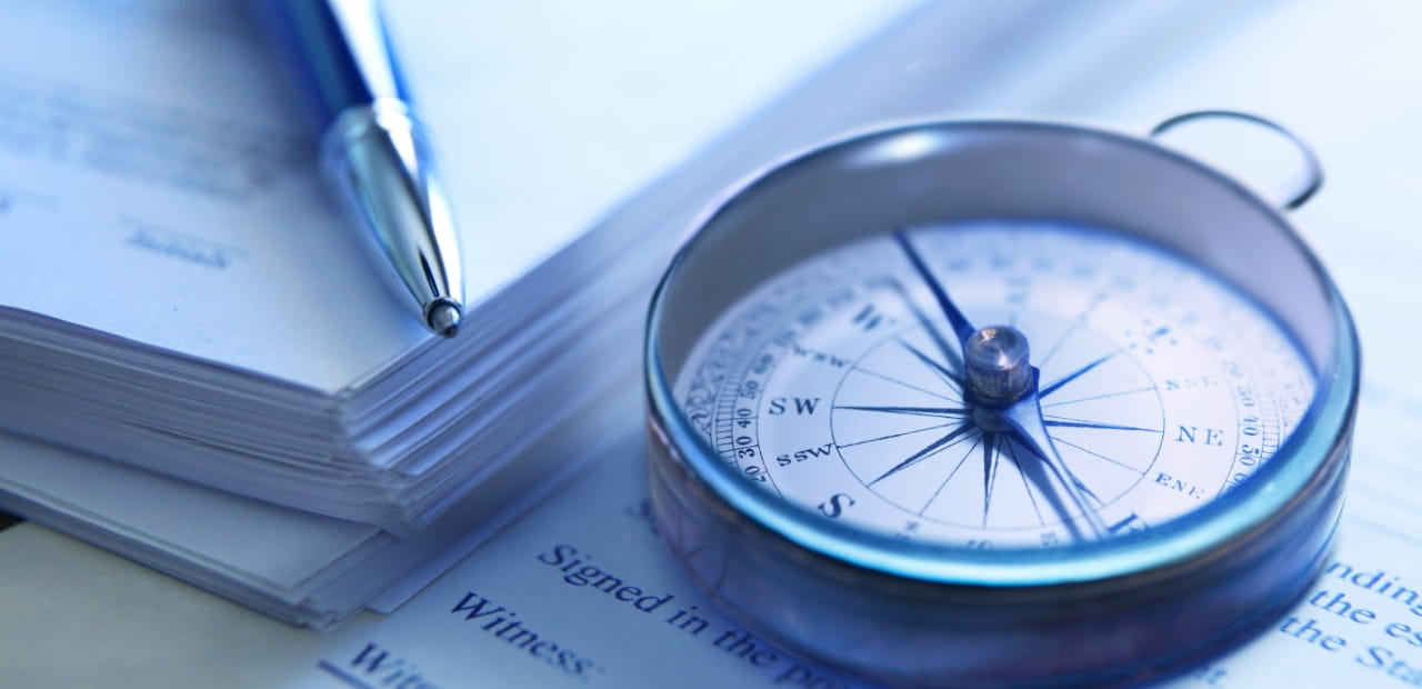 A close-up of a compass and pen resting on a stack of documents.