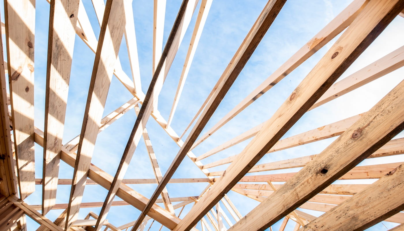 View from below of wooden roof framing against a blue sky.