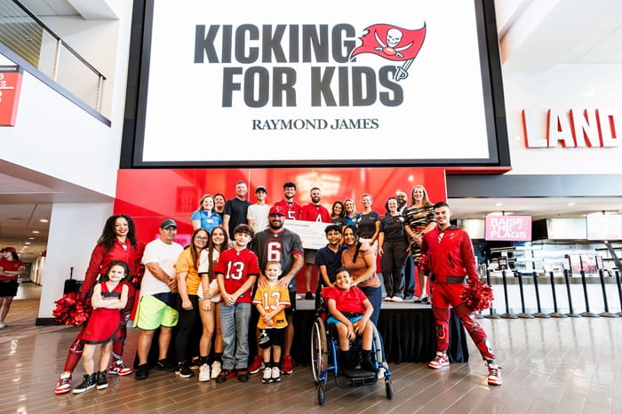 Patients, families, Bucs players, cheerleaders and Raymond James representatives post in front of large Kicking for Kids sign